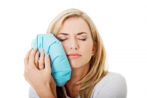 Woman holding ice pack to cheek with eyes closed in pain