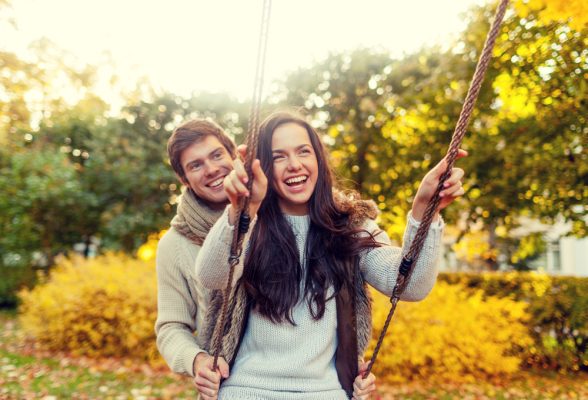 young man and woman on a date outside on a swingset