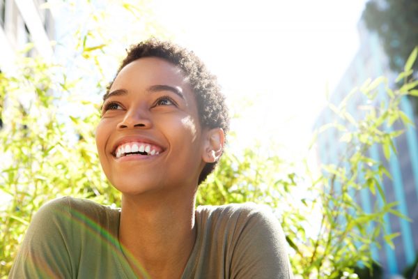 woman with short hair and dark skin smiling while looking up outside